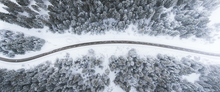 Vinterväg som går genom en snötäckt skog. Bilden är tagen uppifrån.