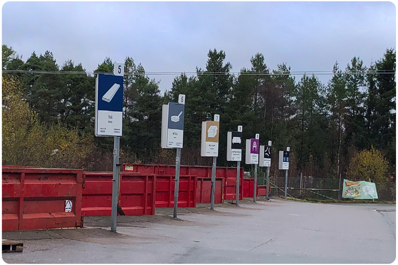 Bild från en av SÅM:s återvinningscentraler, visar röda containrar och grå himmel.
