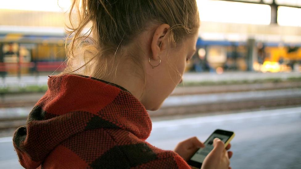 En person använder sin telefon. I bakgrunden syns en tågperrong.